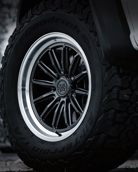 A high-contrast, extreme close-up of a rugged black off-road alloy rim paired with a textured all-terrain tire.
