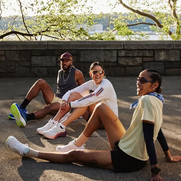 A group of three diverse runners sitting and laughing in a park setting, showcasing running shoes as a lifestyle accessory.