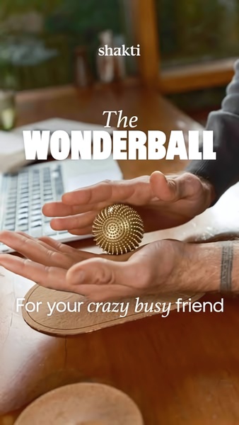 A close-up, high-contrast shot of hands holding a golden, textured acupressure ball with centered, bold typography.