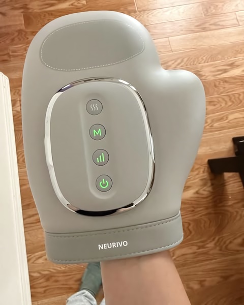 A close-up, first-person perspective of a user holding a grey, heated hand massager with visible interface controls.