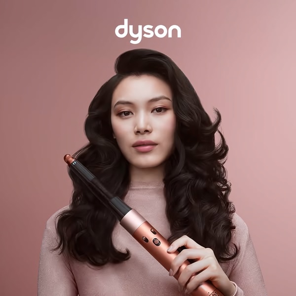 A high-end product hero creative featuring a model holding a professional hair styling tool against a monochromatic pink studio background.
