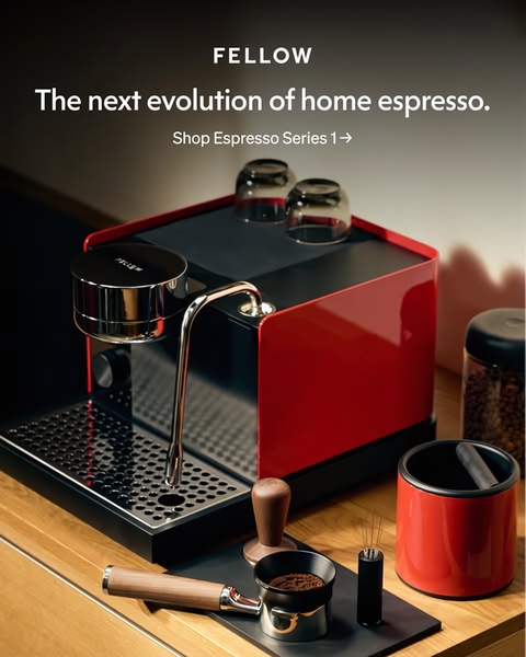 A high-end, studio-lit photograph of a red and black professional-grade espresso machine displayed with premium brewing accessories on a wooden surface.