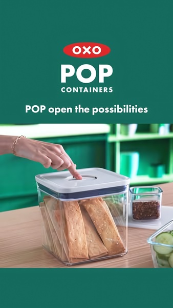 A close-up shot showing a hand pressing the button on a clear food storage container, demonstrating its easy-to-use pop-open mechanism.