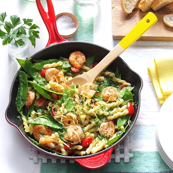 A top-down view of a vibrant shrimp and pasta dish being tossed in a red cast iron skillet, emphasizing fresh ingredients and home-cooked quality.