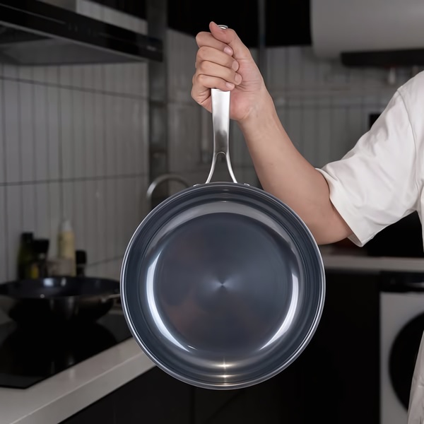 A clean, high-contrast, studio-style shot focusing entirely on the sleek design and high-quality finish of a non-stick frying pan held by a user.
