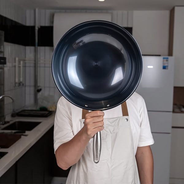 A close-up, centered composition where a frying pan held by a chef completely obscures the person, drawing total focus to the product itself.