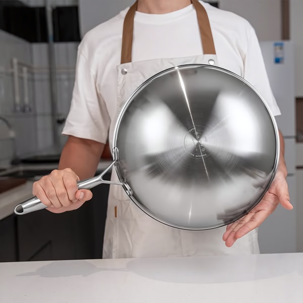 A clean, high-clarity shot of a chef holding a stainless steel wok in a modern kitchen setting.