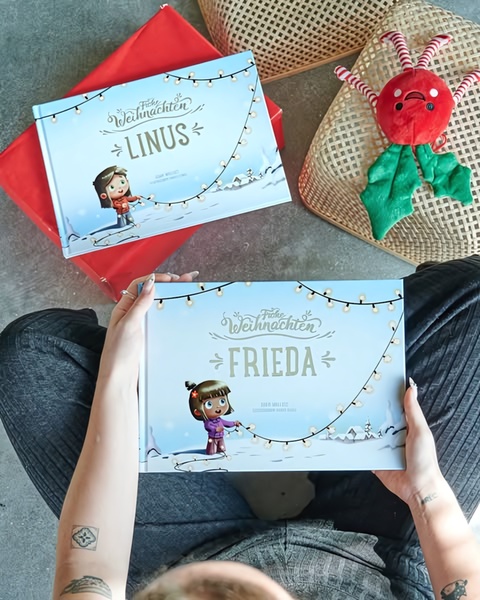 A top-down, first-person perspective photograph featuring two personalized children's books titled with specific names, set against a festive, cozy background.