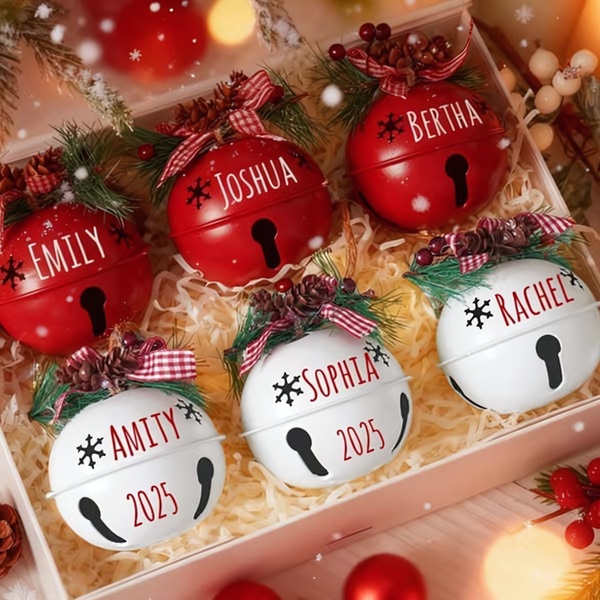A high-angle flat lay shot showcasing multiple custom Christmas bells with individual names and the year 2025 engraved in a gift box.