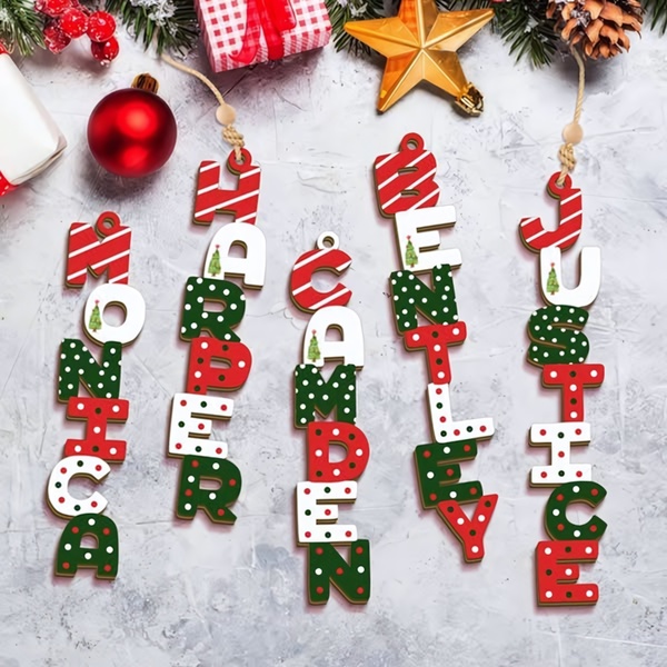 A high-angle, top-down shot of five custom-named Christmas ornaments laid out on a neutral surface with seasonal decorations, emphasizing the product's personalization.
