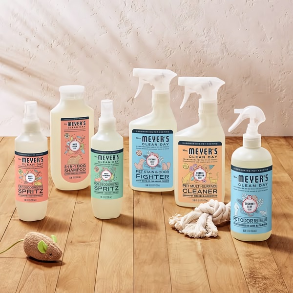 A high-quality 1:1 ratio studio shot showcasing a complete set of pet-friendly cleaning products arranged on a natural wood surface.