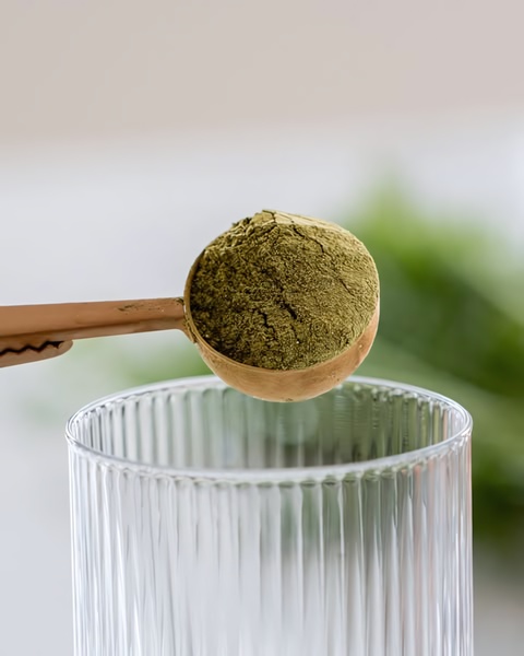 A close-up shot showing a measuring spoon filled with bright green matcha powder over a clean glass, highlighting product purity.