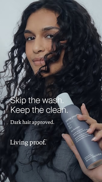 A close-up portrait of a woman holding a bottle of dry shampoo, highlighting a solution for clean hair without washing.
