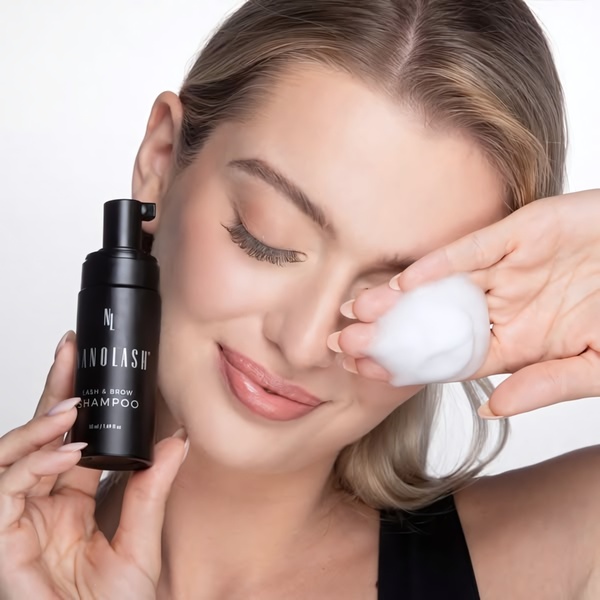 A clean, high-quality product hero shot featuring a model holding the lash shampoo bottle with the product foam visible in her palm.