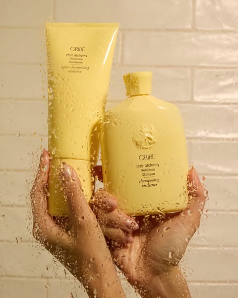 A high-end product hero shot featuring hair shampoo and conditioner bottles viewed through a water-drenched glass surface to evoke freshness and luxury.