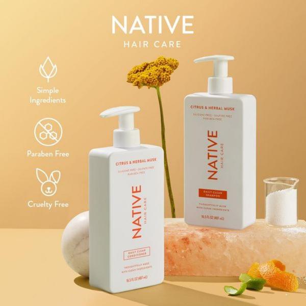 A clean, minimalist product photography shot displaying shampoo and conditioner bottles alongside organic ingredients like citrus and salt crystals.