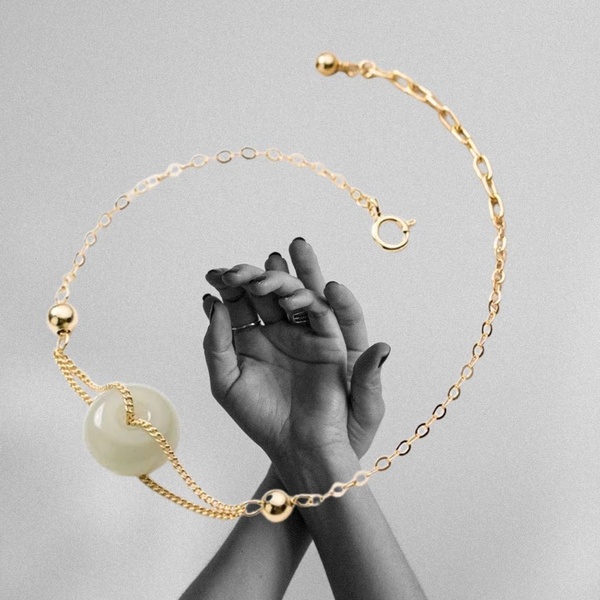 A high-contrast black and white photography creative featuring a jade beaded necklace suspended around hands, emphasizing material texture and luxury.