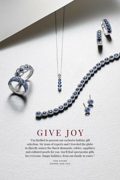 An elegant, high-end flat lay featuring a sapphire and diamond necklace, bracelet, earrings, and rings on a clean, light-reflective surface.