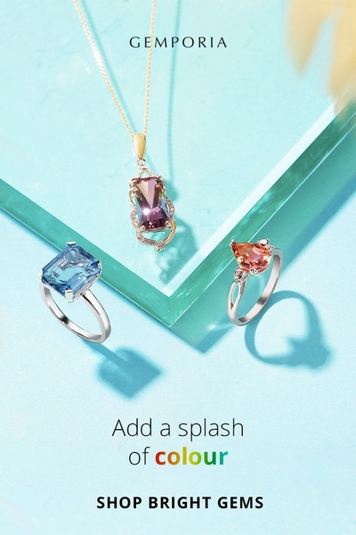 A high-quality studio shot of a jewelry necklace and two rings arranged on a glass surface against a clean light blue background.