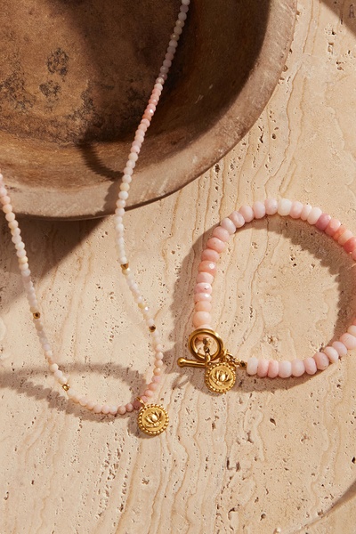 A high-quality product shot featuring a beaded necklace and matching bracelet styled on natural stone, evoking a premium and earthy aesthetic.