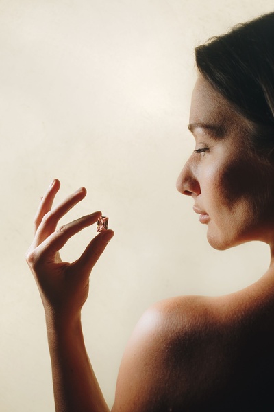 A close-up, high-contrast shot of a model holding a single, small gemstone, emphasizing color and texture through soft lighting.