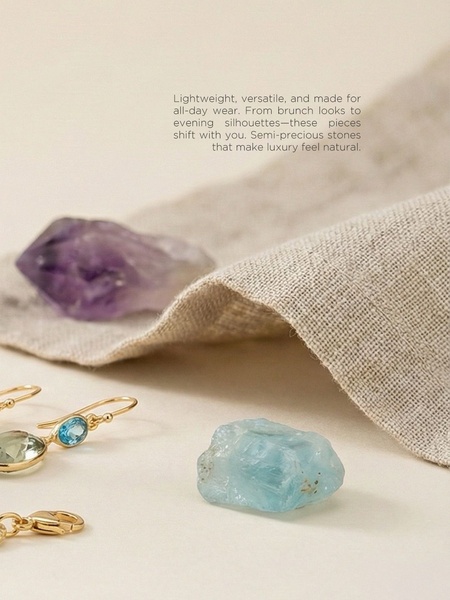 A refined product hero shot featuring semi-precious stones and gold jewelry resting on textured fabric, emphasizing a high-end, organic brand identity.
