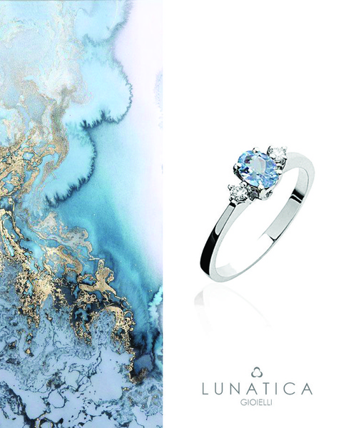 A refined product ad for a three-stone ring, set against a split-screen of abstract liquid blue art and clean white space.