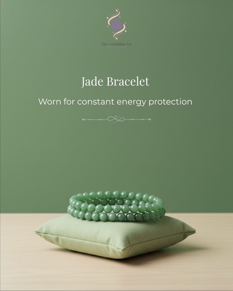 A clean, minimalist product shot featuring a jade bracelet resting on a fabric cushion against a sage green background.