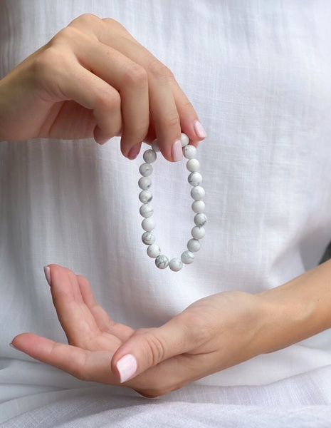A close-up, high-key image of a person's hands delicately holding a stone bead bracelet, emphasizing the texture and simplicity of the product against a neutral white background.
