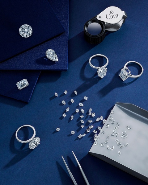 A high-end top-down shot of loose diamonds and diamond rings on a deep blue velvet surface, featuring a jewelers loupe and tweezers.