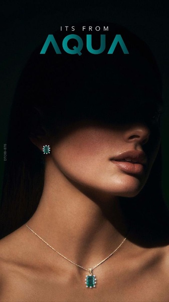 A close-up, dramatic shot focusing on a model wearing a singular emerald pendant and earring, with the brand name at the top.
