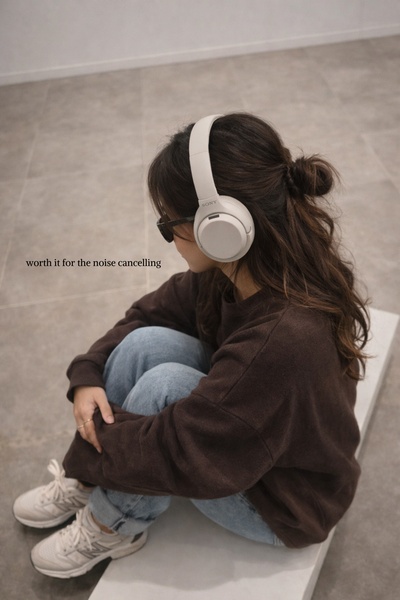 A quiet, candid shot of a user wearing beige noise-cancelling headphones while sitting in a neutral-toned room, emphasizing comfort and focus.