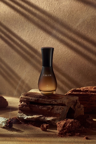 A high-end product photography shot of a perfume bottle centered on a weathered stone ledge, utilizing natural lighting and earthy color palettes.