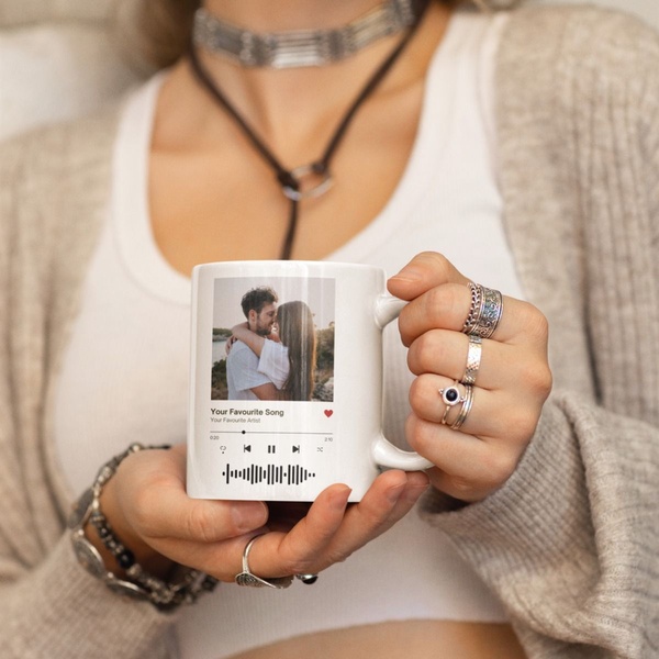 A close-up shot of a customer holding a white ceramic mug featuring a printed photo and a Spotify-style music player UI with a scannable soundwave.