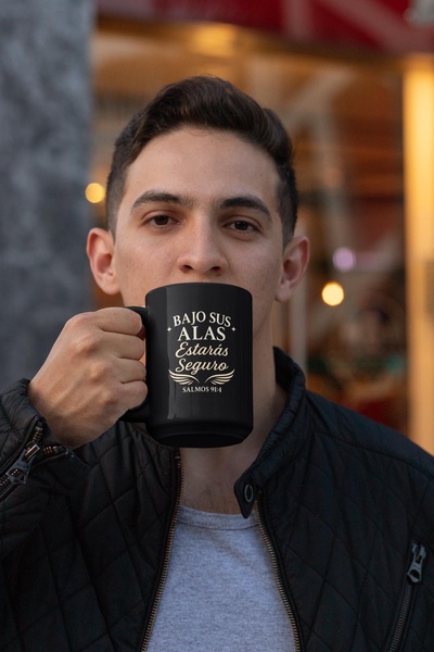 A close-up shot of a man holding a black ceramic mug featuring a religious quote, demonstrating the product in a relatable, daily-use setting.