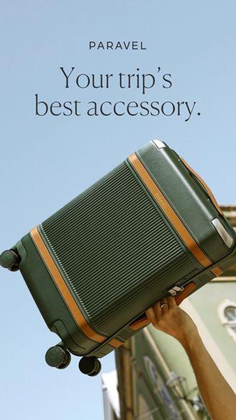 A high-angle, clean product shot of a green suitcase being held against a clear blue sky, positioning it as an essential travel companion.