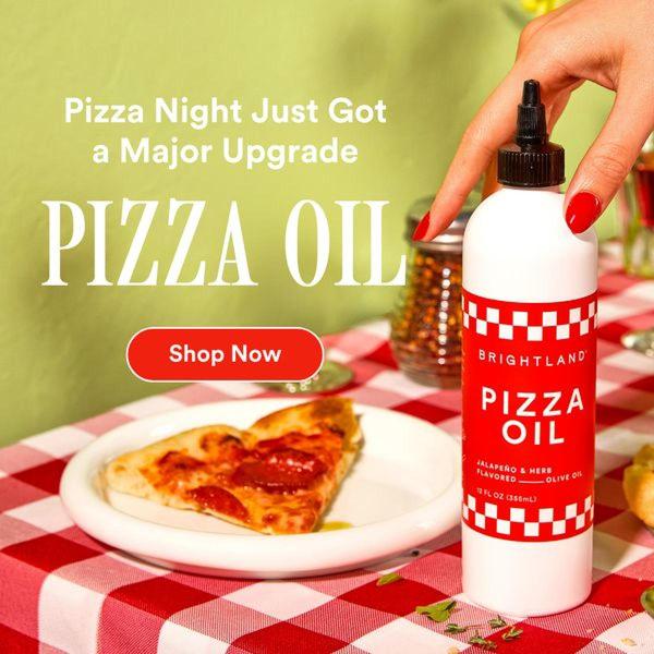 A close-up photograph of a bottle of jalapeño herb pizza oil placed on a red and white checkered tablecloth next to a slice of pepperoni pizza.