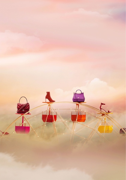 A high-fashion, ethereal visual featuring luxury handbags and shoes displayed on a ferris wheel floating in a dreamy pink cloud landscape.
