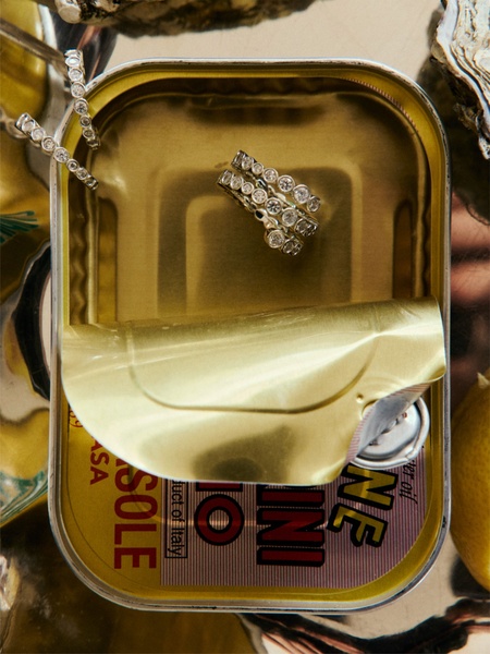 A high-end ring rests inside an opened gold-colored sardine tin, contrasting luxury jewelry with an everyday food item.