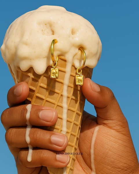 A close-up shot of gold hoop earrings hanging from a melting ice cream cone against a vibrant blue sky.