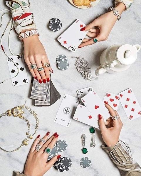 A high-end flat lay featuring intricate jewelry and accessories arranged alongside playing cards and a tea set to evoke a feeling of exclusivity.