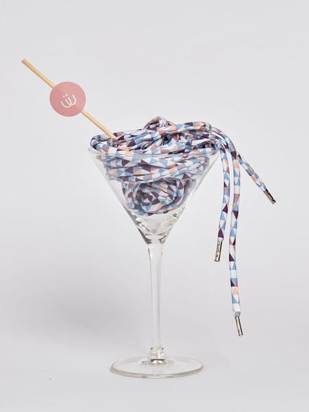 A creative visual display featuring patterned shoelaces coiled inside a martini glass, styled as a sophisticated beverage.