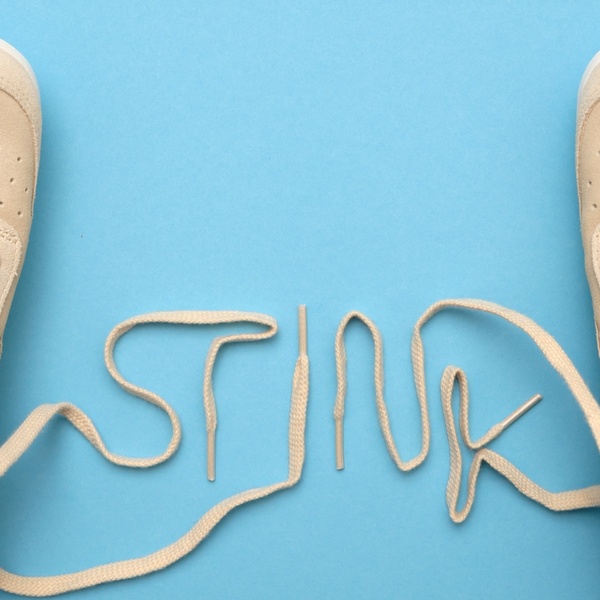 A minimalist ad creative that uses the laces of a pair of beige running shoes to spell out a word on a flat blue background.