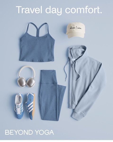 A clean, top-down flat lay composition of an athleisure outfit, including a matching set, cap, and headphones on a light blue background.