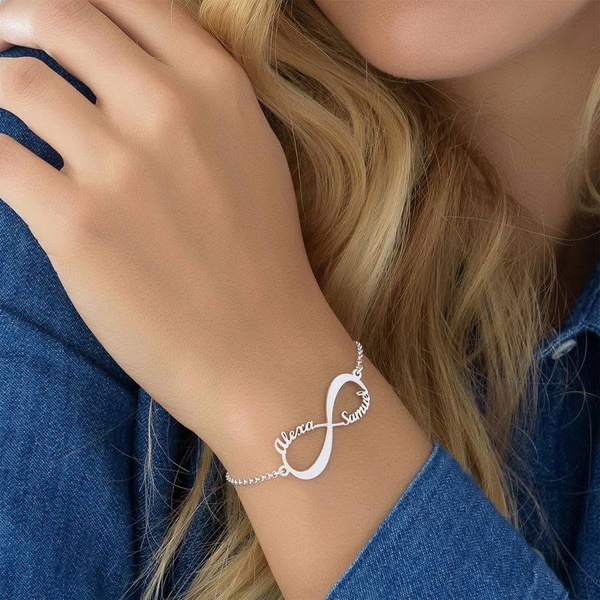 A close-up photograph showcasing a silver personalized infinity bracelet on a woman's wrist, emphasizing delicate detail and custom personalization.