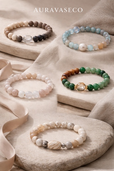A high-end flat lay arrangement of five distinct beaded bracelets on a natural stone surface, emphasizing texture and refined color palettes.