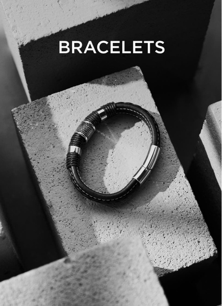 A high-contrast, black and white minimalist product shot featuring a leather and metallic bracelet resting on textured concrete blocks.