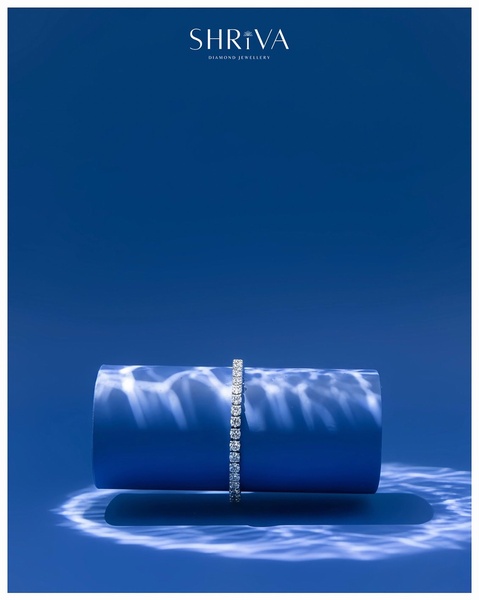A high-end studio capture of a diamond tennis bracelet floating against a bold blue cylindrical background with caustic light reflections.
