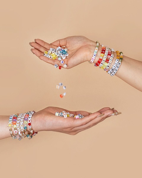 A close-up, minimalist shot featuring two hands holding and scattering colorful lettered beaded bracelets.