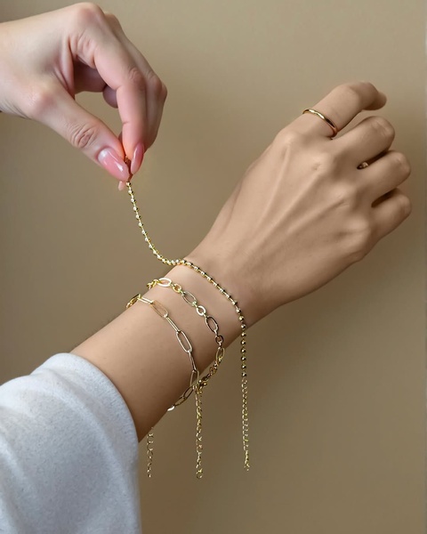 A close-up shot featuring a hand styling three delicate gold chain bracelets against a neutral backdrop.